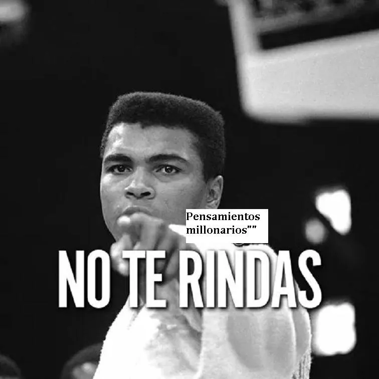 Es una foto en blanco y negro de Muhammad Ali. Está mirando a la cámara con el puño en alto. Lleva una camiseta blanca y un pantalón negro. El fondo es negro.